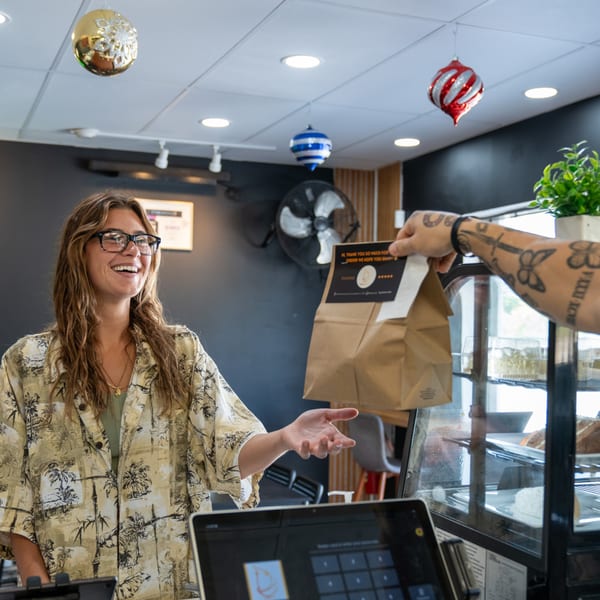 A Holy Bowly employee happily hands a customer a to-go bag with a thank you sticker.