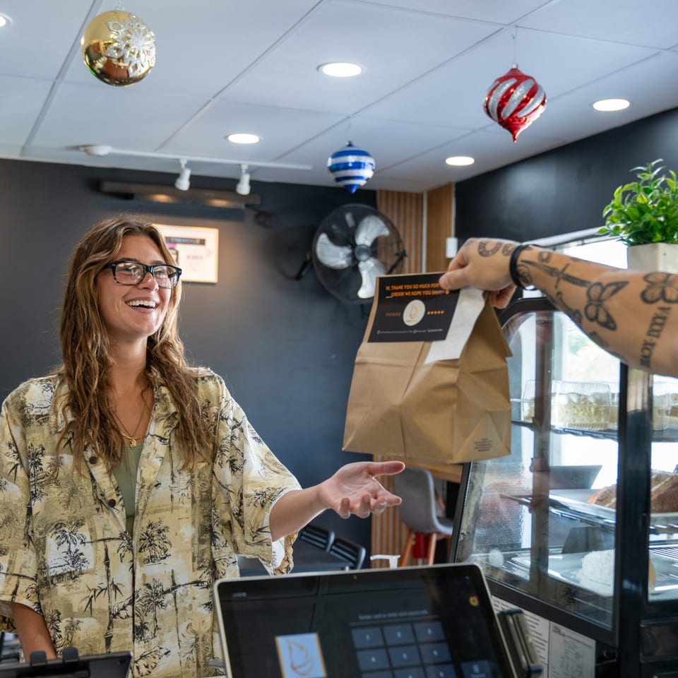 A Holy Bowly employee happily hands a customer a to-go bag with a thank you sticker.